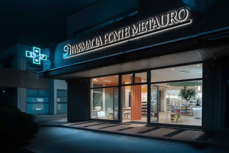 Vista esterna della farmacia illuminata di notte con insegna e vetrate trasparenti