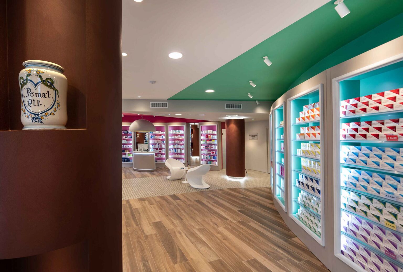 Ingresso farmacia con esposizione prodotti retroilluminata, pavimento effetto legno e area accoglienza sul fondo