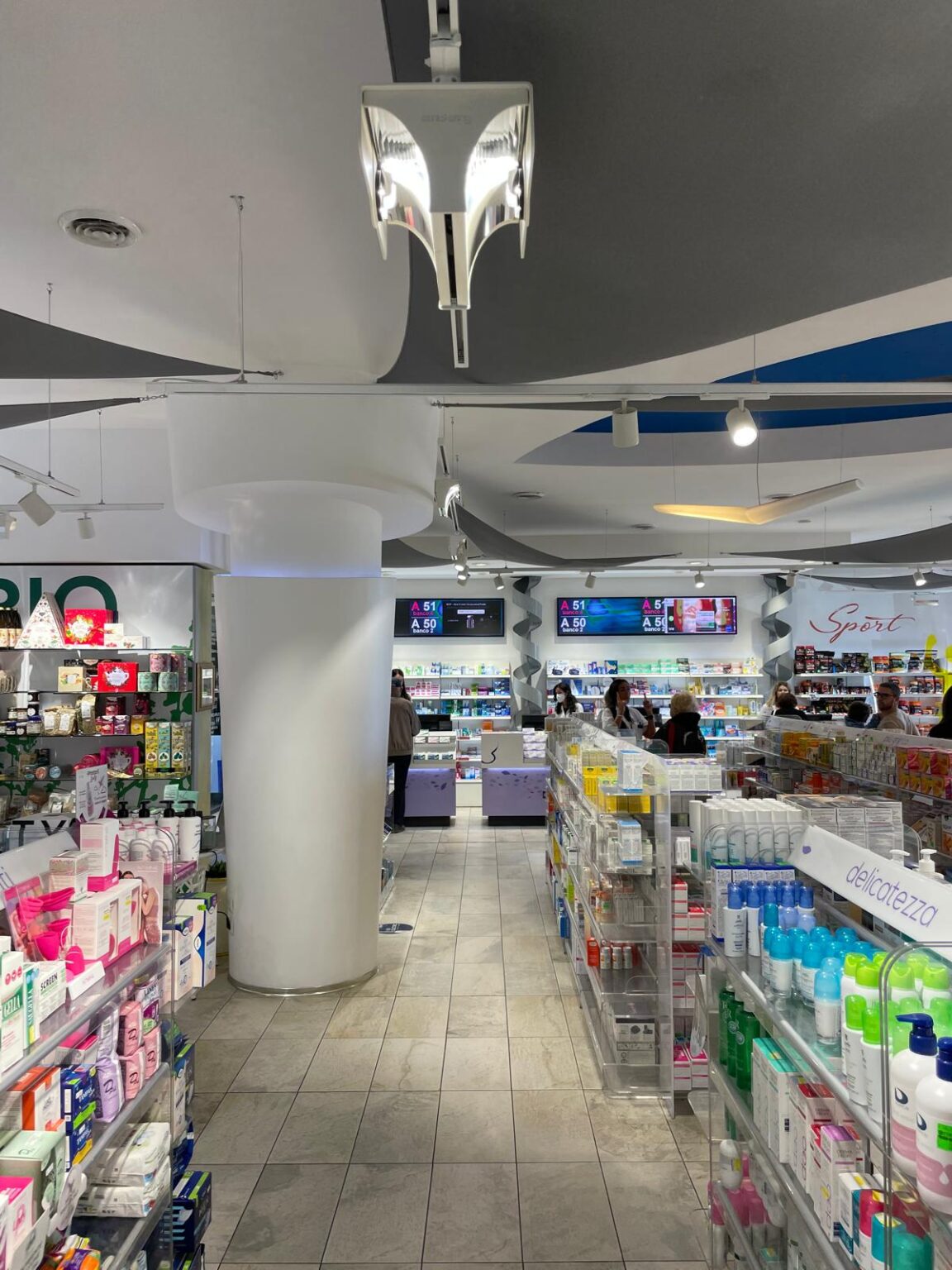 Corsia centrale con esposizione ordinata dei prodotti e area banco sullo sfondo in un layout funzionale e fluido